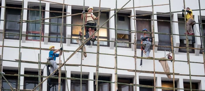 Stavební dělníci pracují na lešení z bambusu u budovy.
