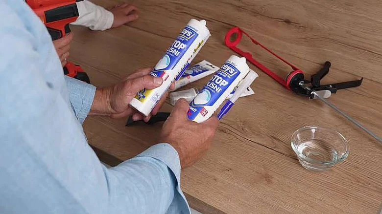 Dvě tuby silikonu s pistolkou na aplikaci kolem vany.