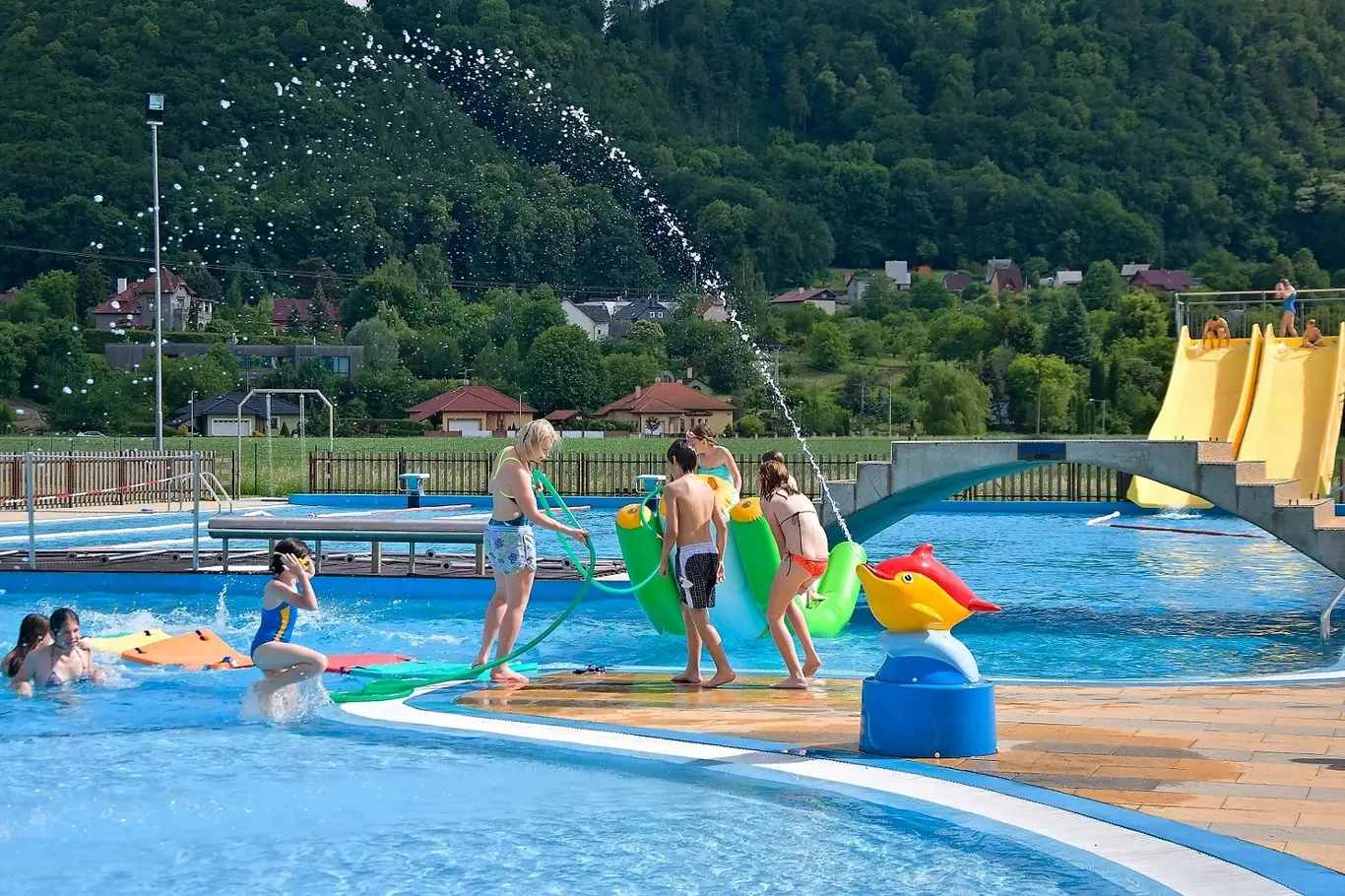Děti se hrají v bazénu s vodními atrakcemi na venkovském koupališti.