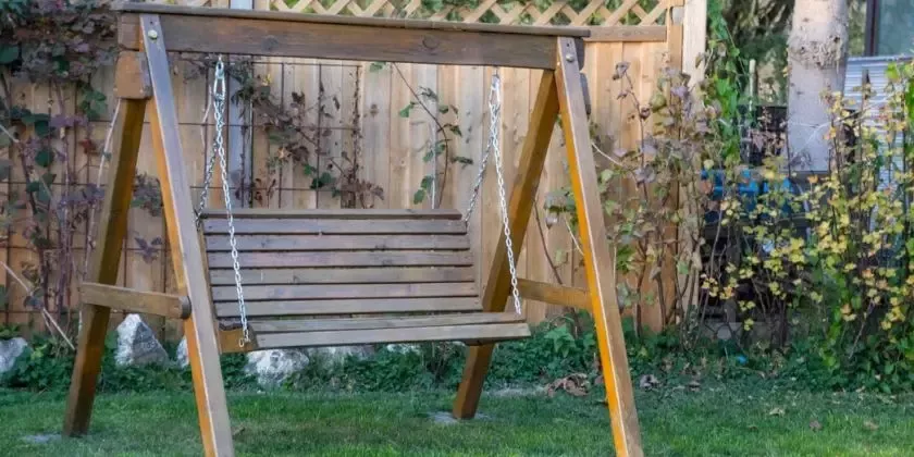 Hotová dřevěná houpačka na zahradu před plotem.