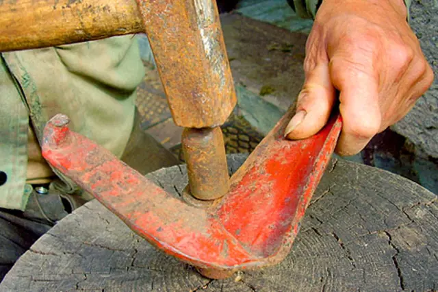 Ruce drží červený nástroj pro broušení sekyrky na dřevěném podkladu.