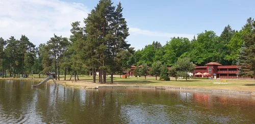 Venkovní koupaliště s jezerem a stromy v okolí.