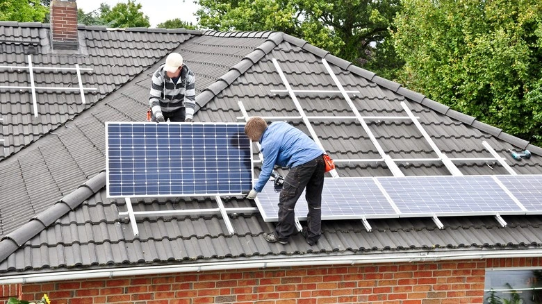 Dva muži montují fotovoltaické panely na střechu domu.