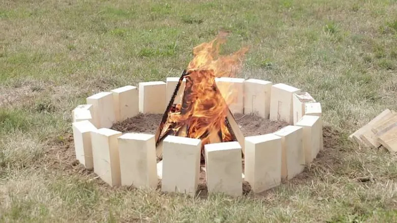Hotová ohniště z cihel s hořícím dřevem na trávníku.