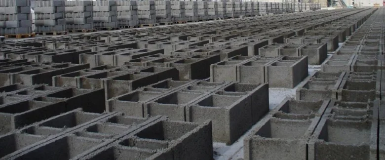 Řady betonových dutých bloků v bednění na výrobním místě.