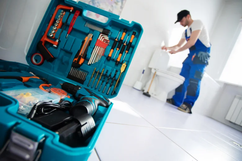 Plumber opravuje záchod s nářadím v modrém kufru.