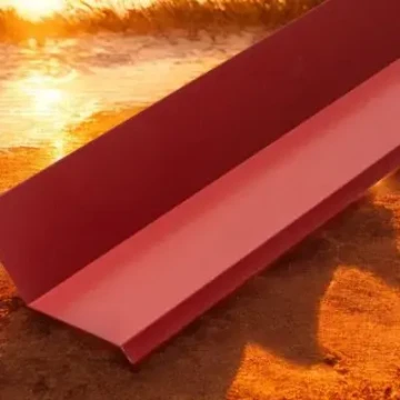 Červený kovový střešní prvek na písečné zemi.