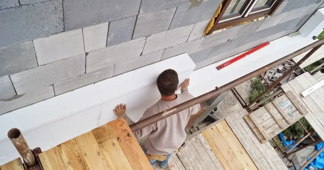 Stavebník montuje izolační desku z polystyrénu na fasádu.