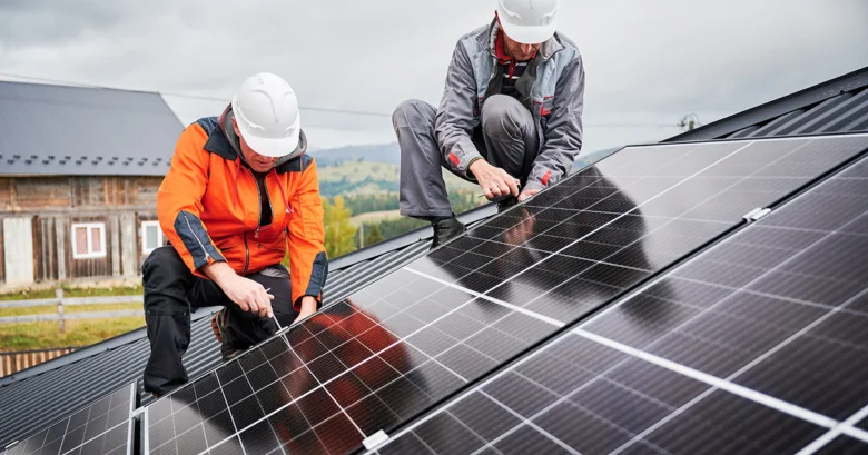 Dva pracovníci montují fotovoltaické panely na střechu.