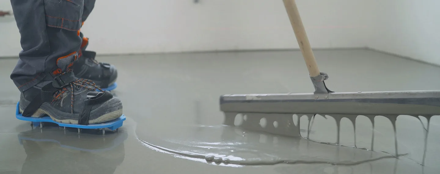 Práce na podlaze: vyrovnávání mokré betonu špachtlí.