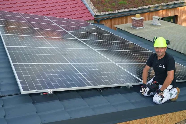Muž montuje fotovoltaické panely na střechu při stavbě svépomocí.