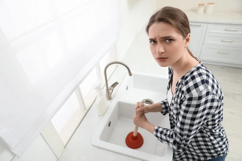 Žena používá hadicový válec k vyčištění zaneseného kuchyňského odpadu.
