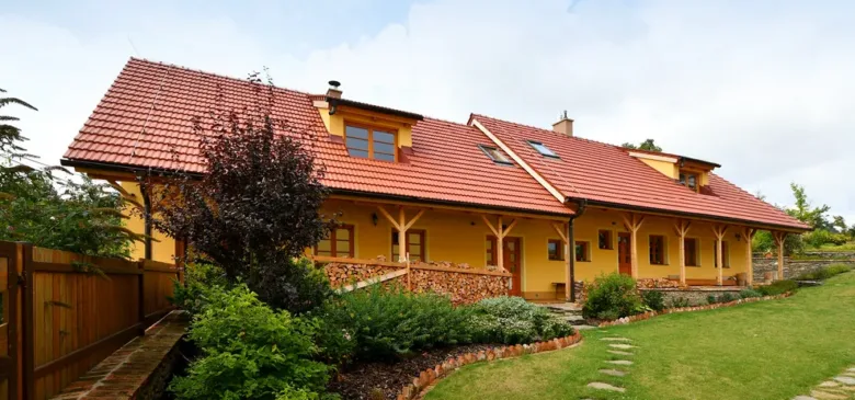Žlutý dům s červenou keramickou střešní krytinou na pozadí zelené zahrady.