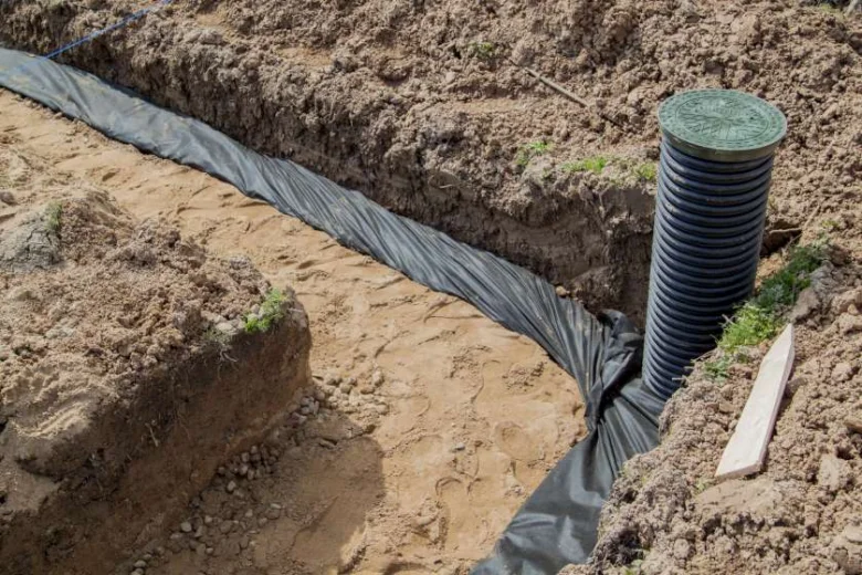 Instalace drenážní trubky v příkopu s geotextilním filtrem.