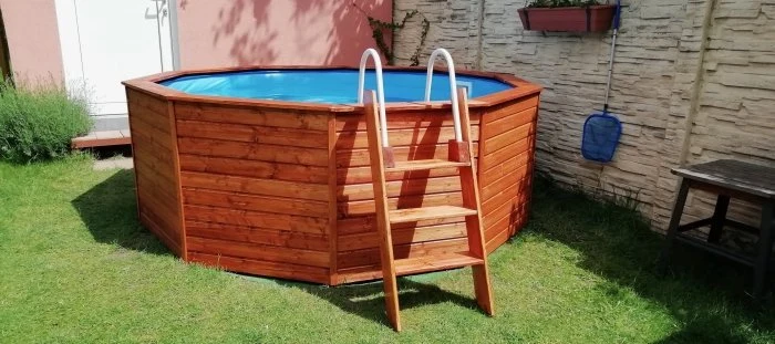 Dřevěný nadzemní bazén s obložení na trávníku u zdi.