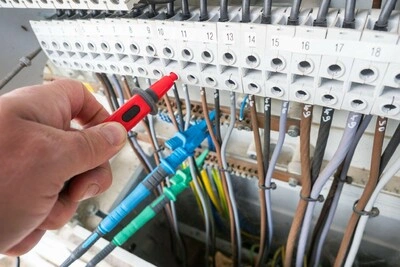 Ruční měření napětí na elektrickém rozvaděči pro revizi instalace.