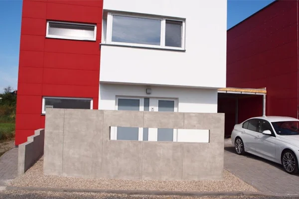 Pohledový beton na plot před domem s bílými okny.