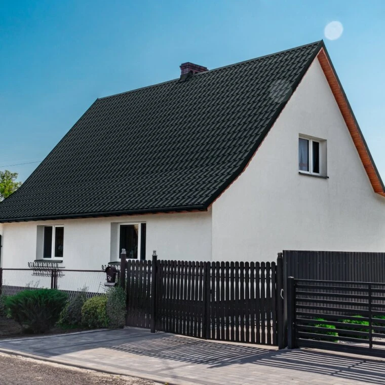 Modern dům s bílou fasádou a černým obezděním před domem.