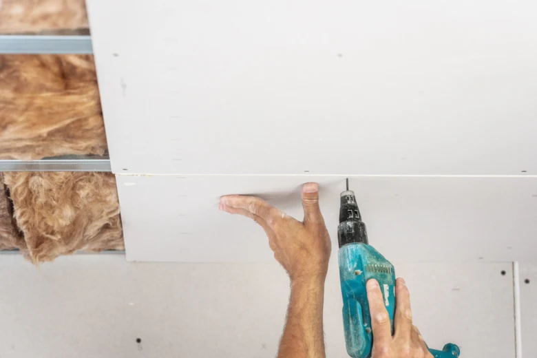 Muž vrtá do sádrokartonu rukojetí vrtačkou při instalaci stropu.