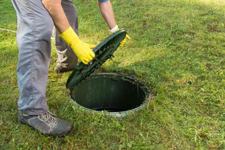 Pracovník otevírá poklop septiku na trávníku.