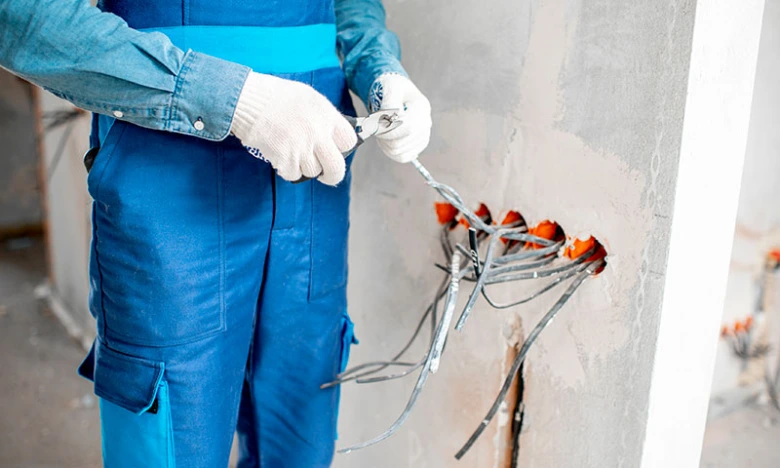 Elektrikář odstraňuje izolaci kabelů ze stěnových otvorů.