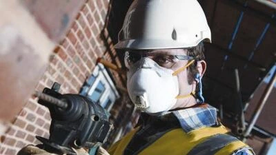 Stavebník v ochranném vybavení s nářadím u cihlové zdi.