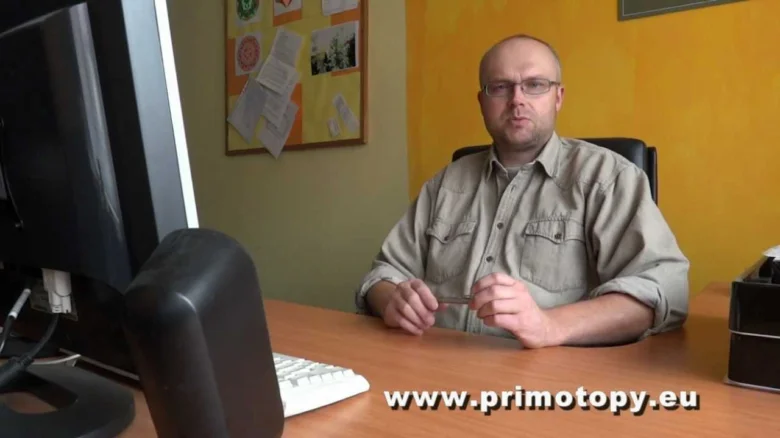 Muž sedící u počítače v kanceláři s textem na obrazovce.