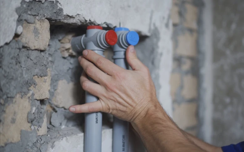 Ruční instalace plastových vodovodních trubek s červenými a modrými uzávěry.