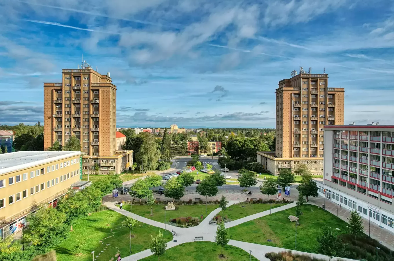 Dvě velké panelové budovy obklopují zelený park v městské čtvrti.