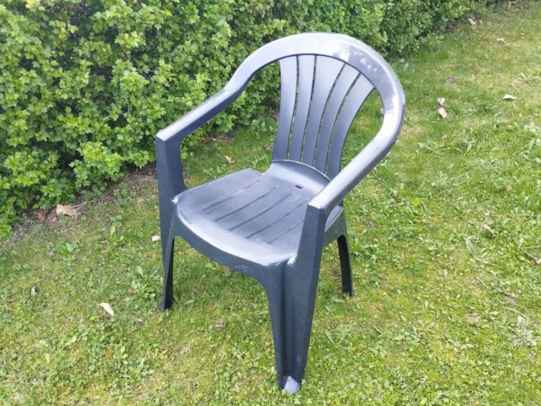 Tmavé plastové zahradní křeslo na trávníku u keře.