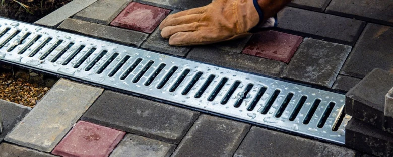 Instalace kovového odvodňovacího žlabu mezi dlažební kostkami.