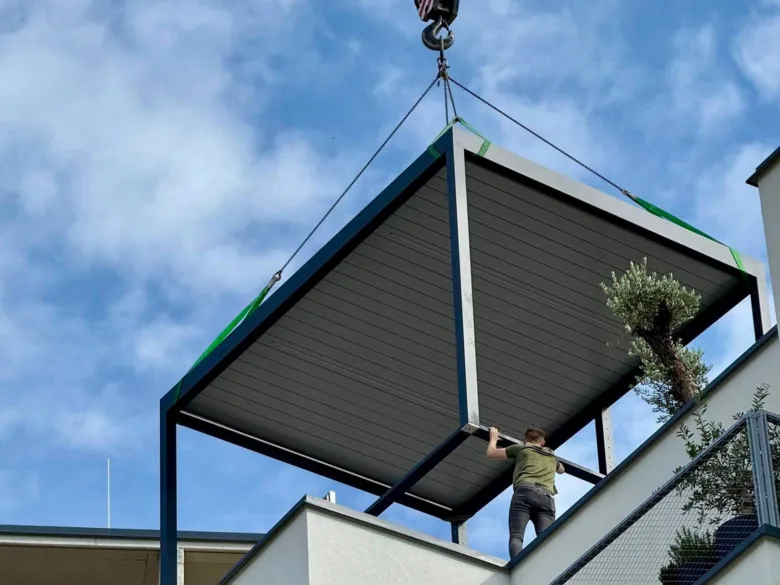 Pergola se zvedá kranem na střechu domu s pracovníkem.