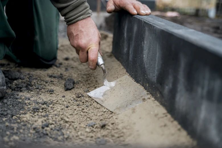 Ruční práce s betonovým obrubníkem při pokládce na zemi.