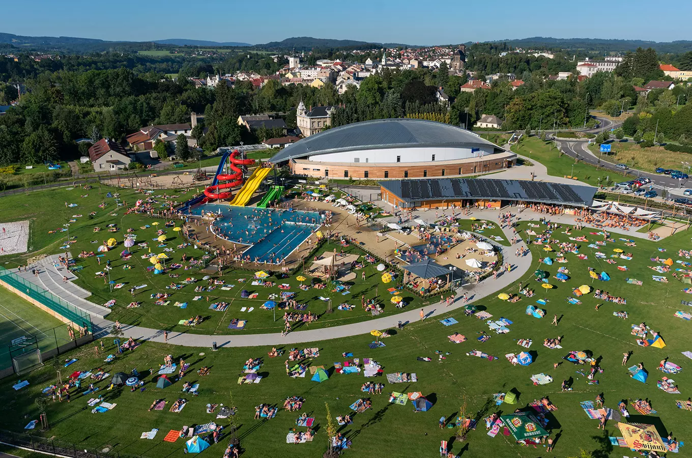 Vzdušný pohled na koupaliště v Turnově s bazénem, skluzavkami a slunečníkem.