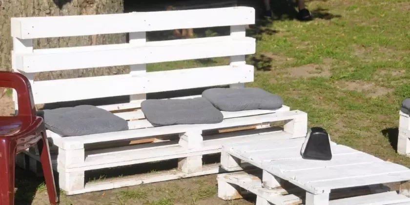 Bílá zahradní lavice z palet s polštáři na trávníku.