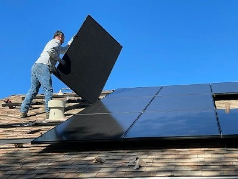 Muž instaluje fotovoltaický panel na střechu domu.
