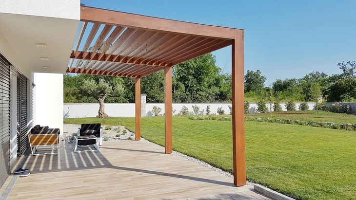 Moderní dřevěná pergola na terase u domu s trávníkem.