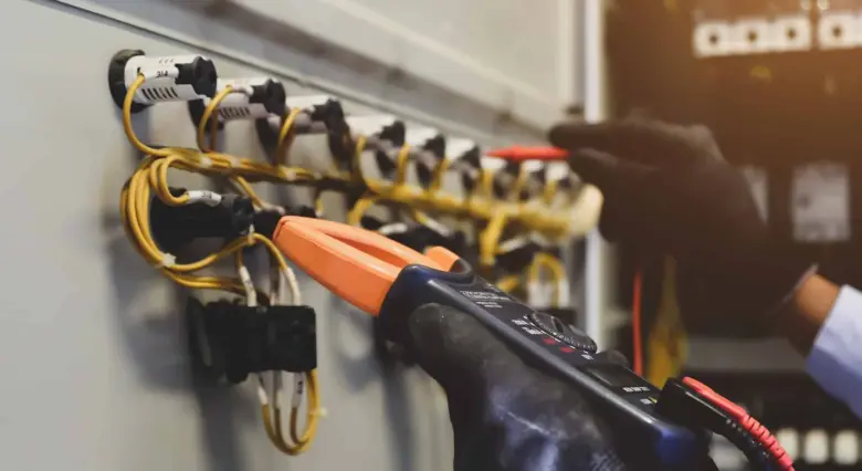 Elektrikář měří napětí žlutých kabelů v rozvaděči pomocí multimetru.