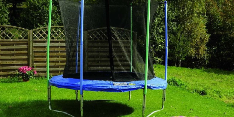 Modrá trampolína s mříží na trávníku u plotu.