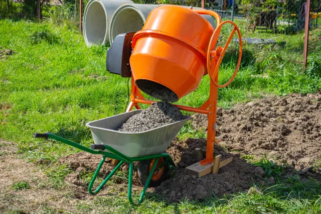 Oranžový betonová míchačka nalévá směs do vozíku.