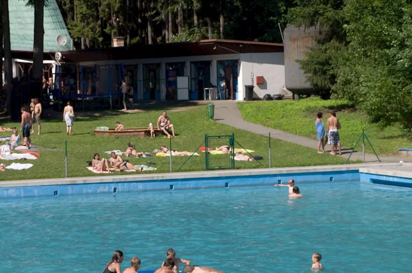 Venkovní bazén v Sloupi s lidmi plavajícími a opalující se.