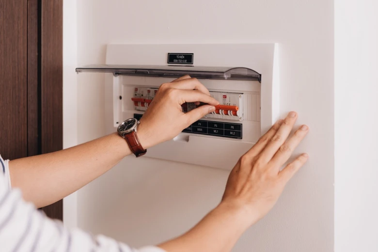 Ruka nastavuje jistič v elektrickém rozvaděči na zdi.