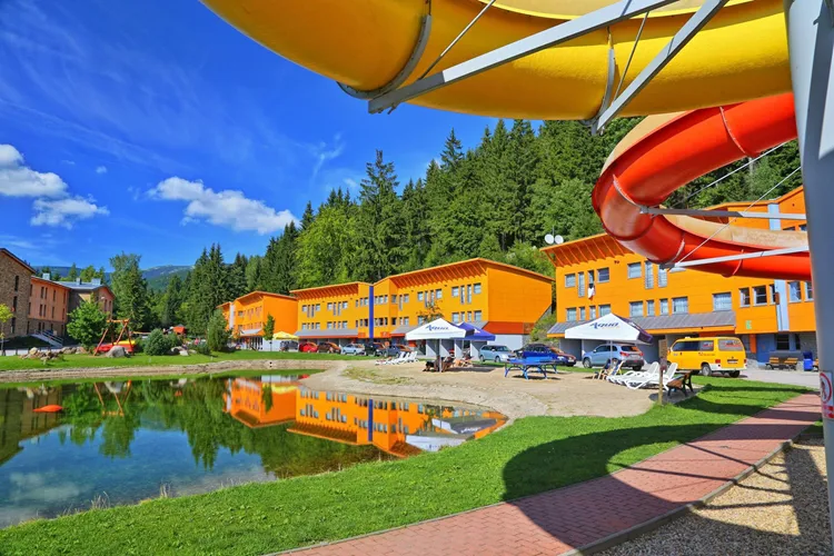 Aquapark ve Špindlerově Mlýně s vodními skluzavkami a oranžovými budovami.