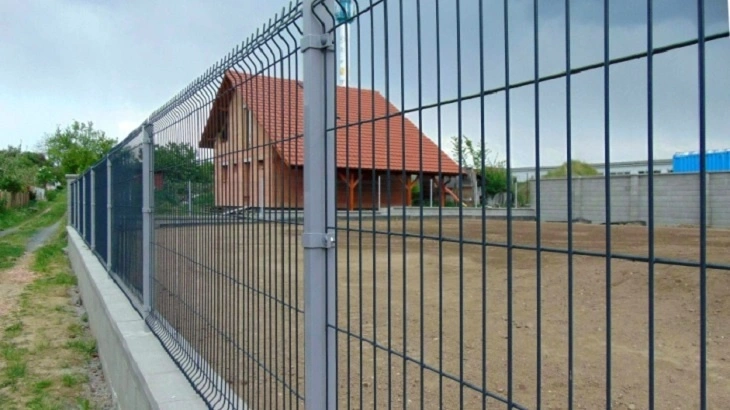 Ocelová plot kolem domu s dřevěnou fasádou.