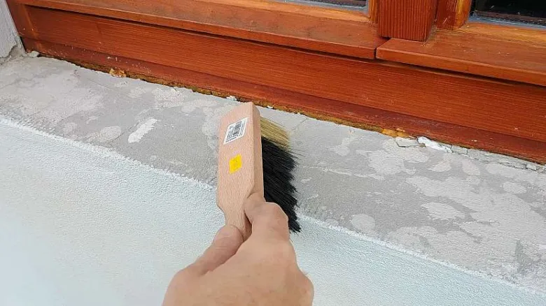 Ruka čistí podokenní desku před montáží vnitřního parapetu.