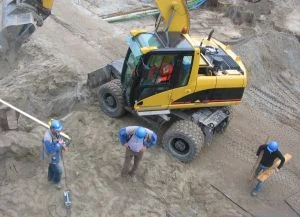 Stavební dělníci u žlutého kopáčka na staveništi.