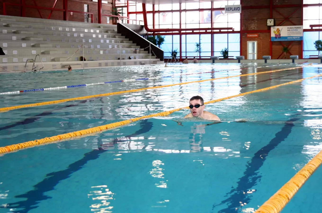 Muž plave v bazénu s tribunami na pozadí.