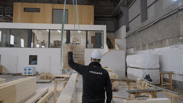Stavebník zvedá dřevěný modul pro stavbu prefabrikovaného domu.
