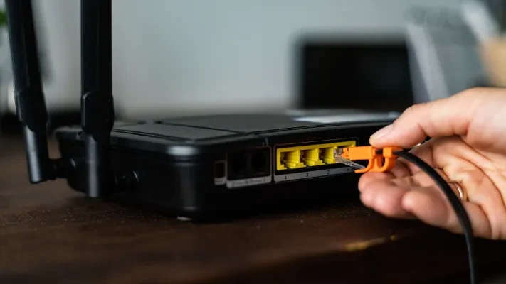 Ruka zapojuje ethernetový kabel do portu na Wi-Fi routéru.