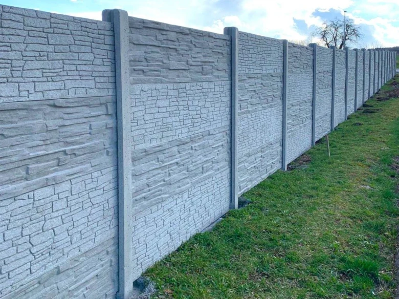 Dlouhá řada šedých pohledových betonových panelů na plotě v exteriéru.